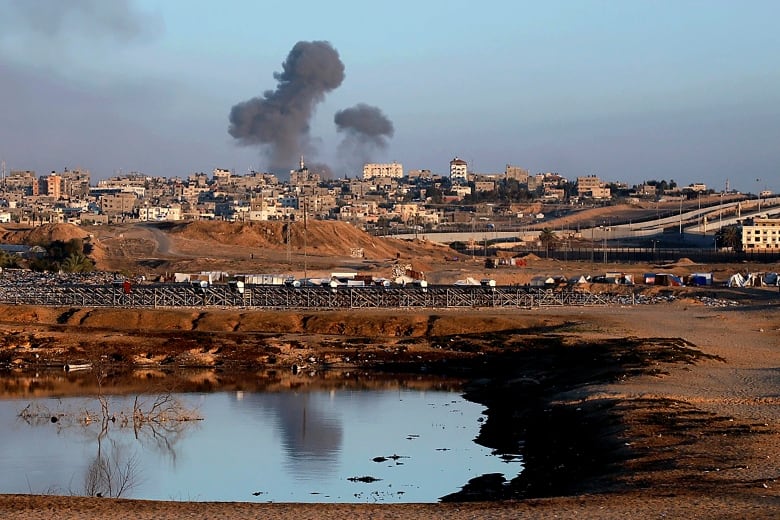 Plumes of dark smoke rise from an urban landscape during the day.