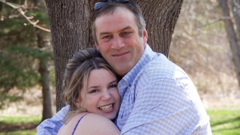 An older man hugs a younger woman wearing a formal blue dress. He has sunglasses on the top of his head. 