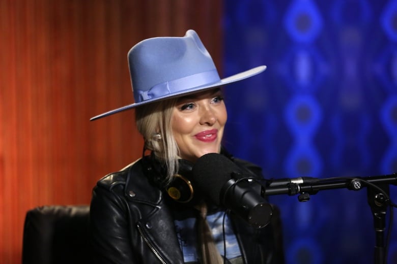 Headshot of a smiling woman, the country singer MacKenzie Porter, wearing a light blue hat with a studio microphone in front of her.