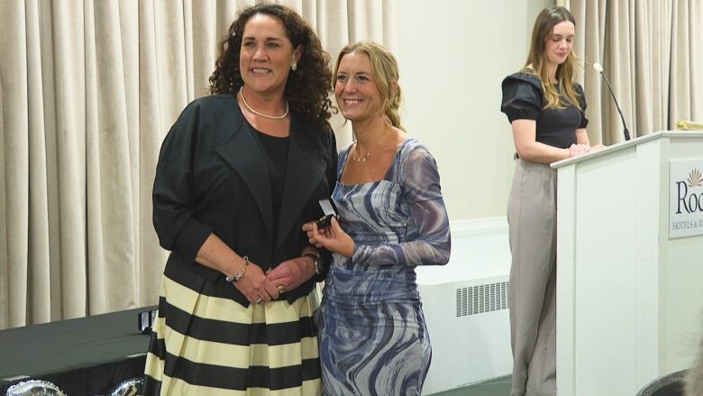 Two women standing in front of another woman at a podium.