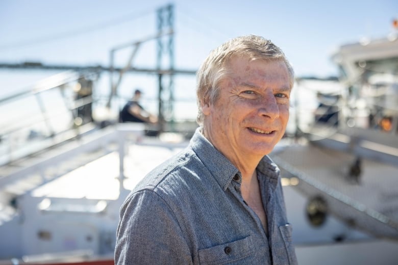 A man with short grey hair and wearing a button-up shirt smiles at the camera.