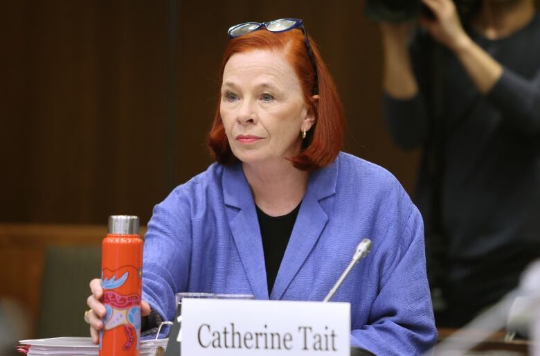 A woman in a lavender blazer sets a water bottle down onto a table.