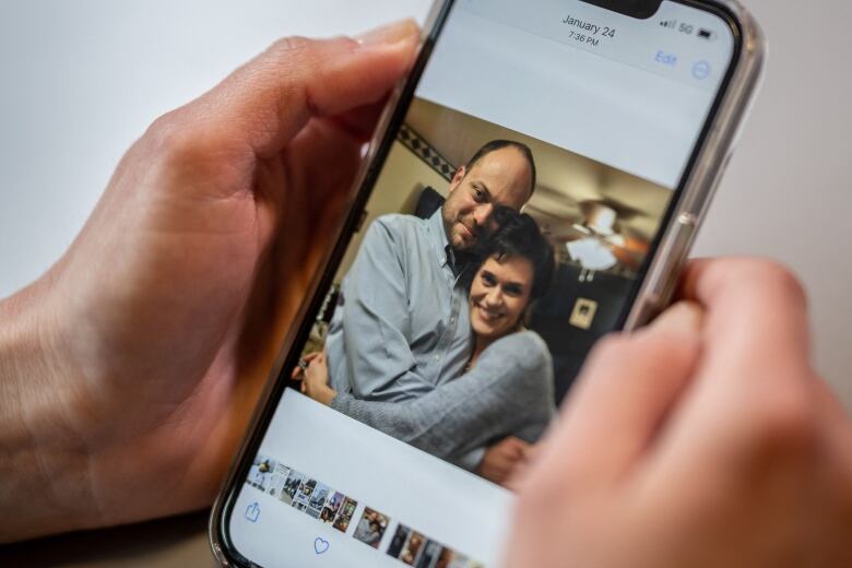 A pair of hands hold a smartphone showing a picture of a smiling, hugging couple 