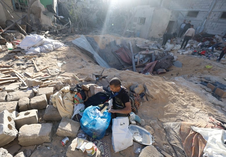 A man kneels on the ground next to a crater where a home used to stand.