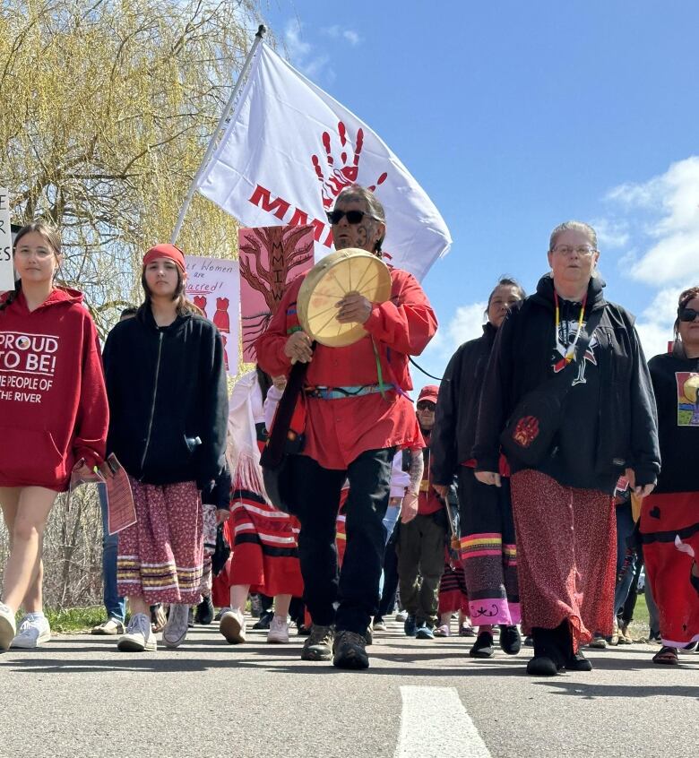 A crowd of people wearing red march down a sunny street.