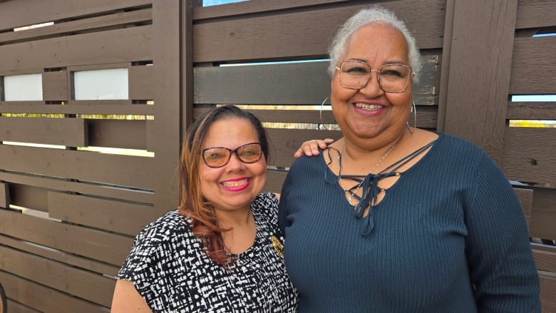 Two women stand outside together and smile for a photo.