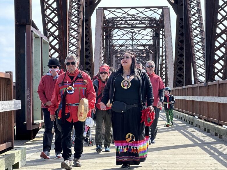 A group of people wearing red walk across a bridge on a sunny day.