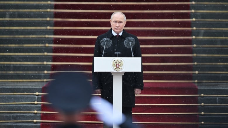 A man wearing a dark coat stands at a podium.