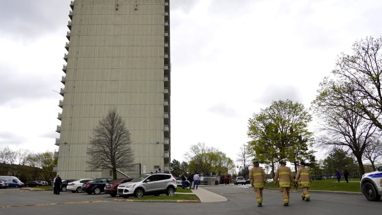 Firefighters walk toward a highrise apartment that just had a fire extinguished.