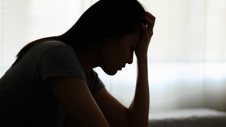 A silhouette of a woman in a dark room holding her forehead in one hand.