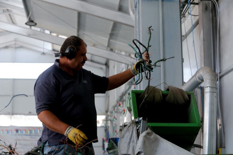 A man with ear protection and gloves holds some cables above a green chute.