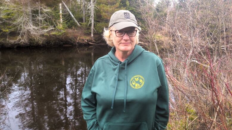 A woman wearing a baseball cap stands with a river in the background 