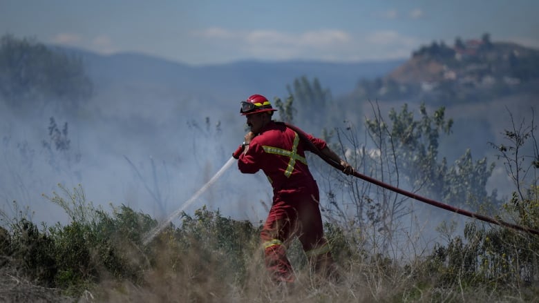 A firefighter in a red suit walks through a smoky field. 