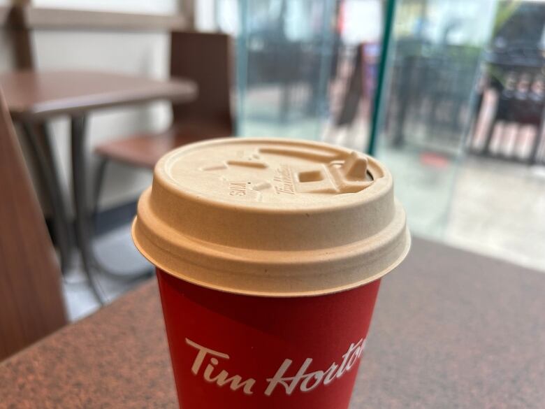 A red Tim Hortons coffee cup stands on a table facing a window.