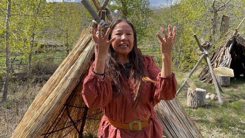 Woman in red with her hands up stand in front of a small lean-to structure