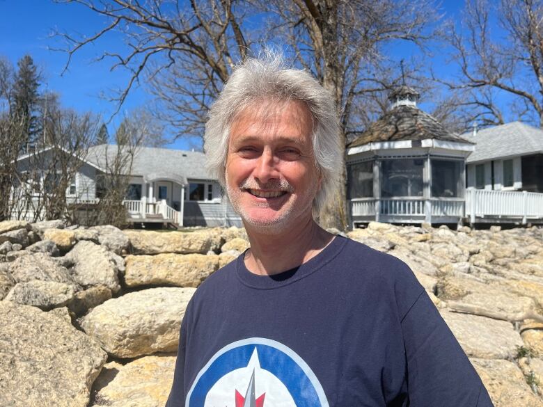 A man standing in front of a rock wall, with his cottage in the background.