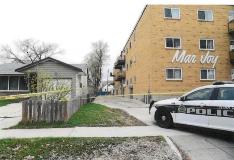 Police tape and a police cruiser are seen parked outside an apartment.