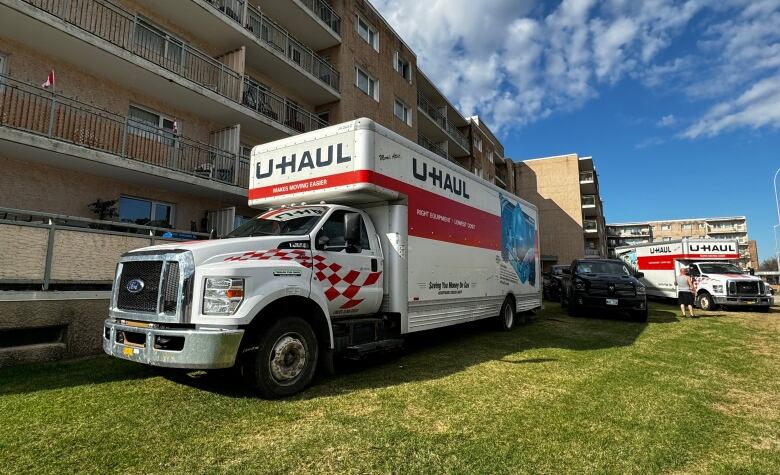 Moving trucks are parked on grass beside an apartment building.