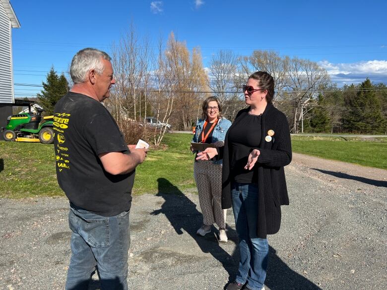 two NDP representatives speak to a man in his yard 