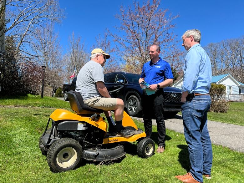 a man sits on his law mower listening to two PC representatives 