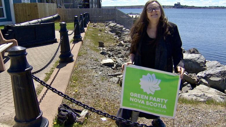 a woman green representative stands with a sign 