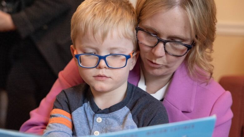 A mother holds her son as the two look at a book together.