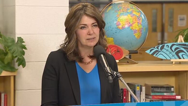 Premier Danielle Smith standing at a podium inside of a library