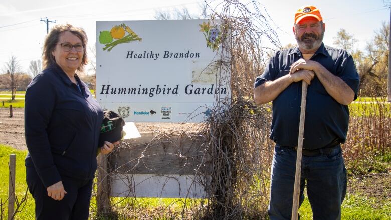 A man and woman stand by a sign that says Hummingbird Garden.