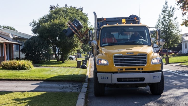 A garbage truck with a robotic arm lifts a can off the curb.