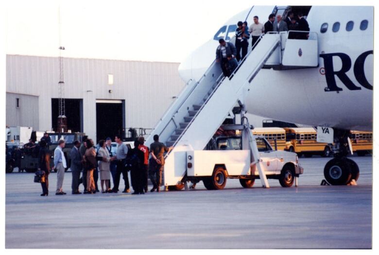 A group of people walk down aircraft stairs to a tarmac,