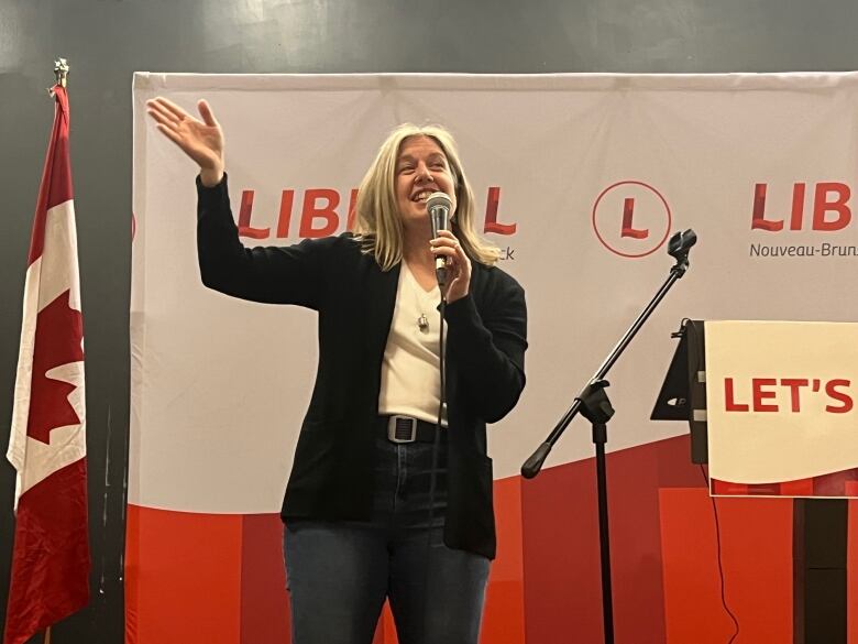 A woman waves in front of a Liberal sign.