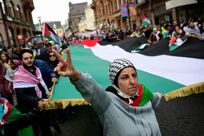 A demonstrator gestures the peace sign as they hold a large flag with other protestors during a march.