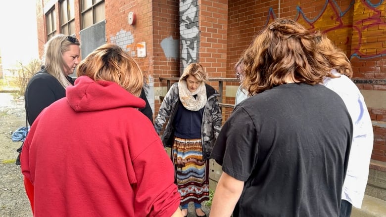 A group of people hold hands in a circle with their heads bowed.