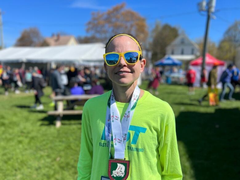 A person wearing yellow glasses, a bright green shirt and a medal is pictured under blue skies. 