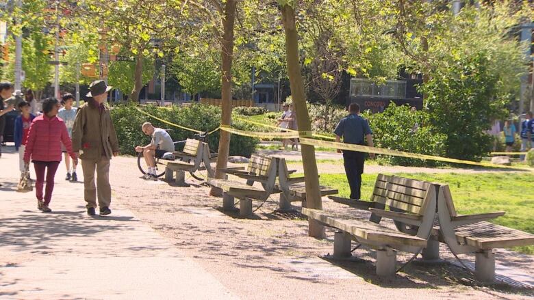 People look toward police officers and a taped off section of a park. 