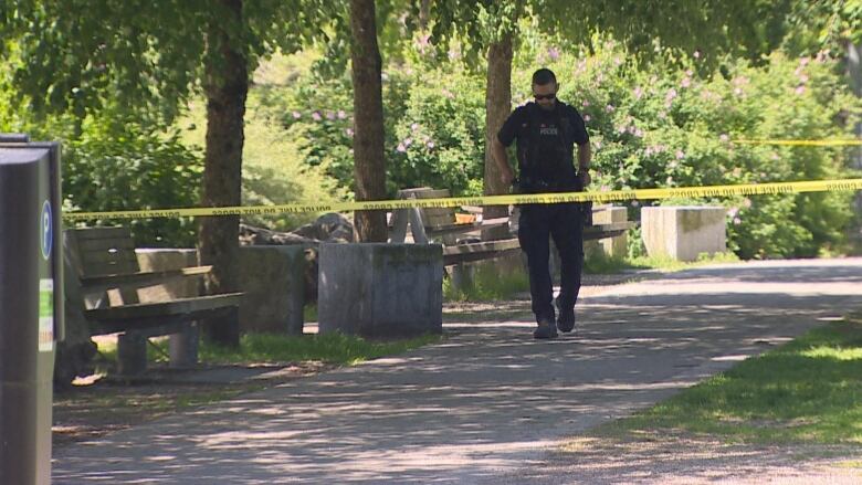 A police officer is pictured walking in a park behind yellow tape. 