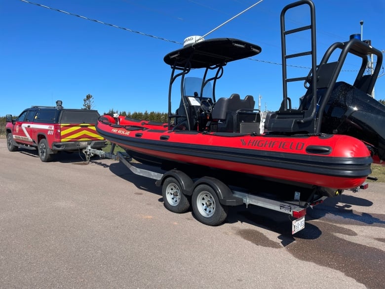 A red Zodiac rescue boat on a trailer hooked to the back of a red fire department pickup truck.