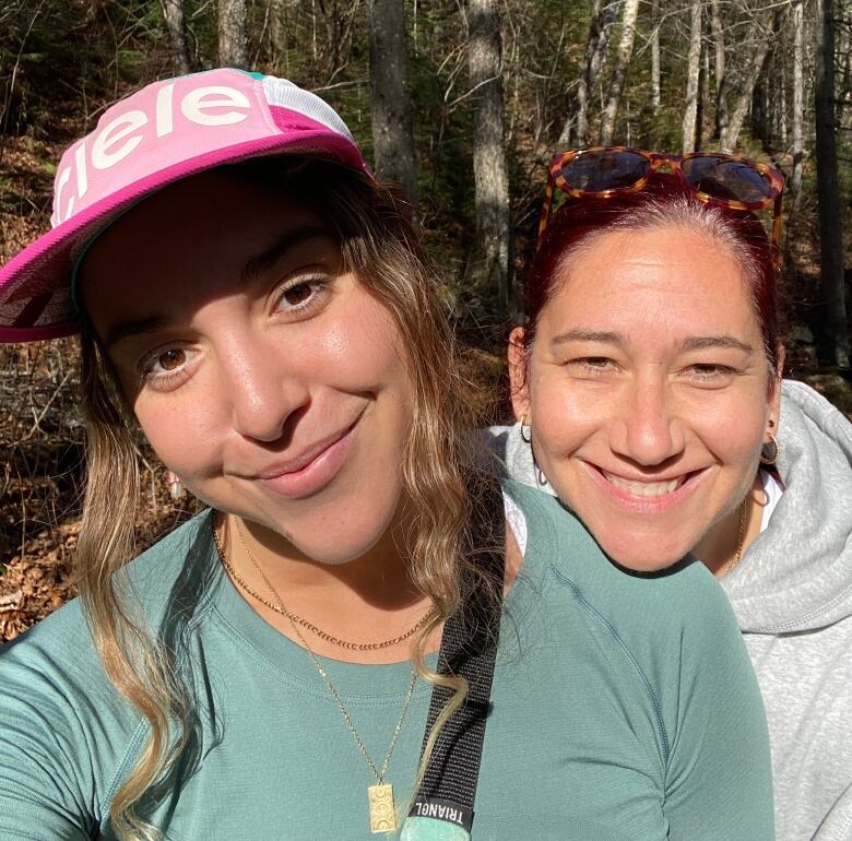 A young woman smiling for a selfie with her mother in the woods. 