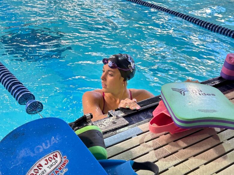 A young woman in an indoor pool with goggles and a bathing cap.