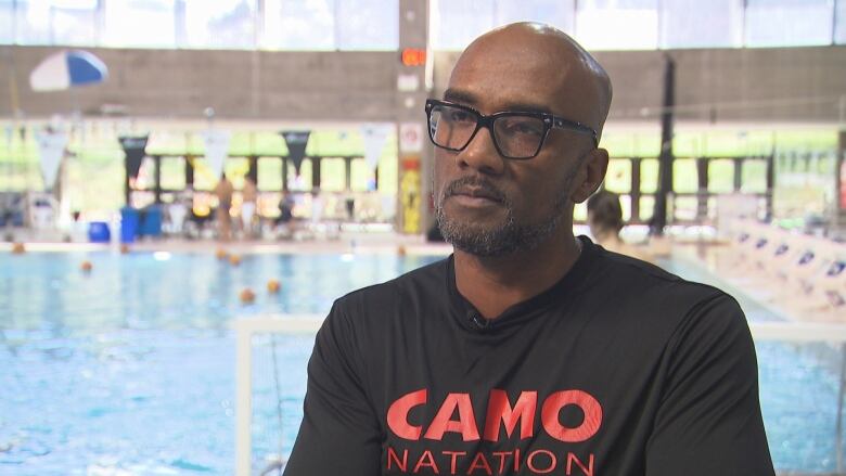 A man stands poolside by an indoor swimming pool. 