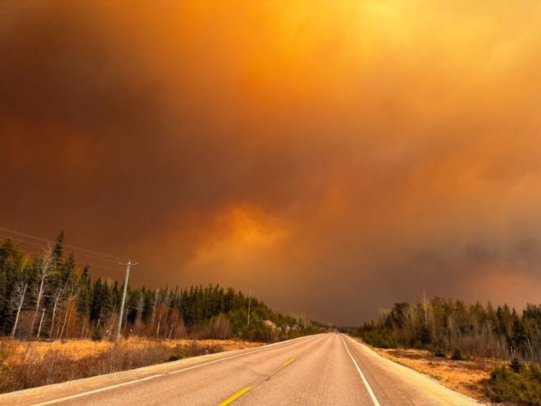 The sky above a highway is black and grey and orange with smoke from forest fires. 