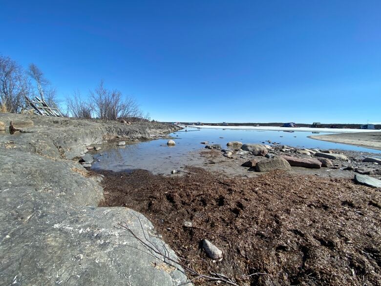 Looking from a rocky muddy shoreline toward a big lake. 