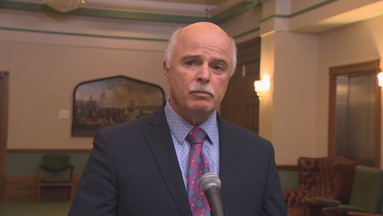 A man wearing a suit stands in the scrum area of Confederation Building.