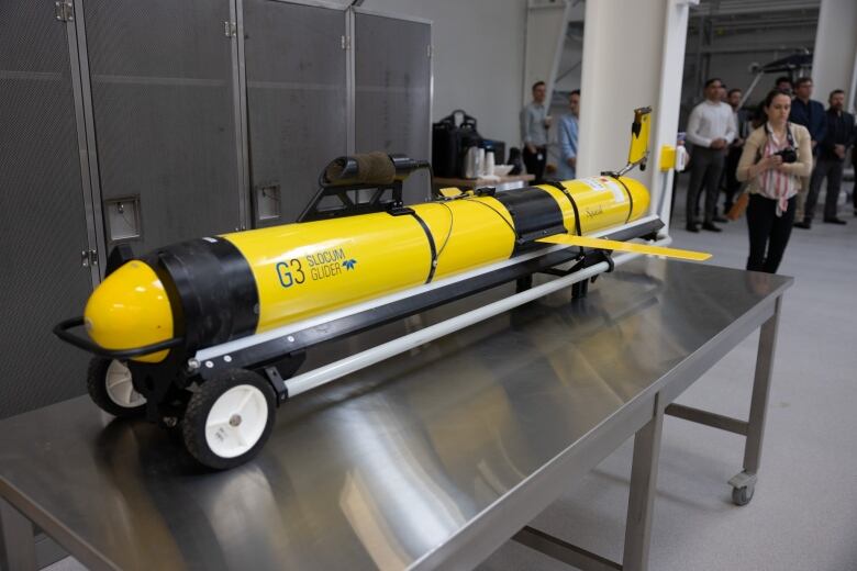 A yellow machine, shaped like a rocket, is seen on top of a metal table. 