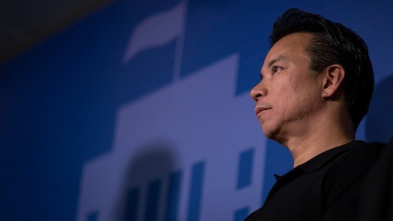 A man looks out with a blue motif of the Vancouver City Hall building flying a flag on the wall behind him.