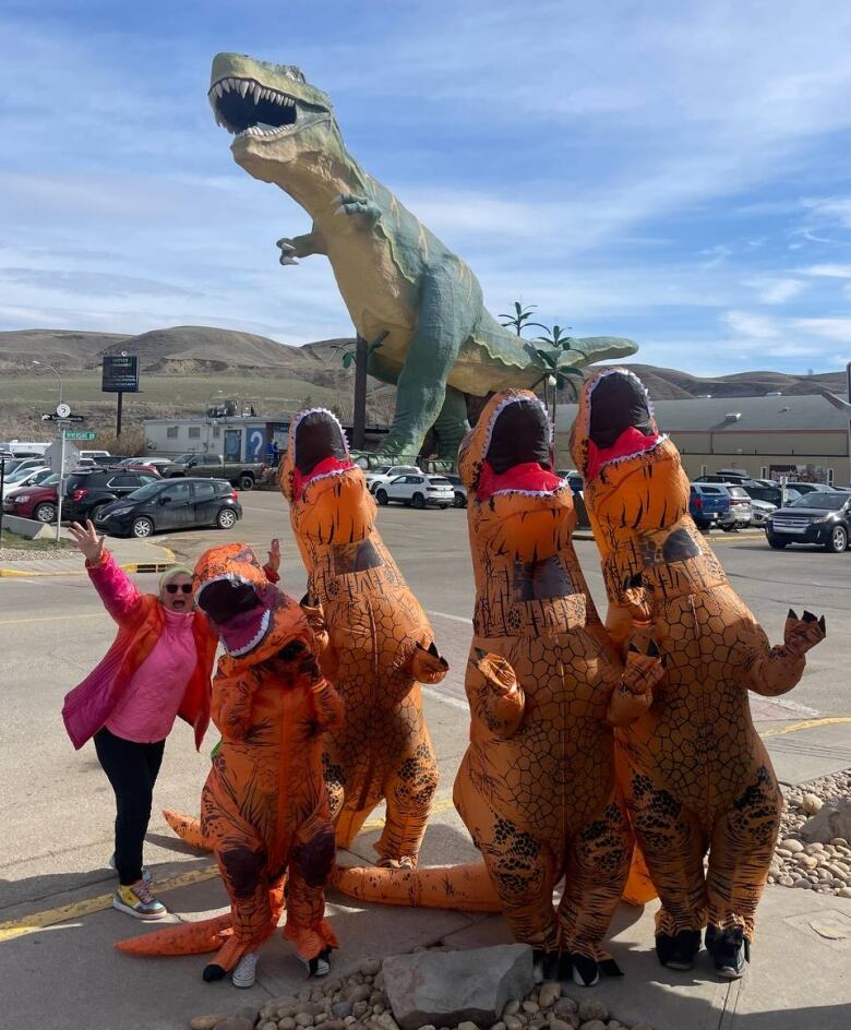 Four people in inflatable dinosaur costumes stand in front of the famous Tyrannosaurus Rex statute in Drumheller, Alta.