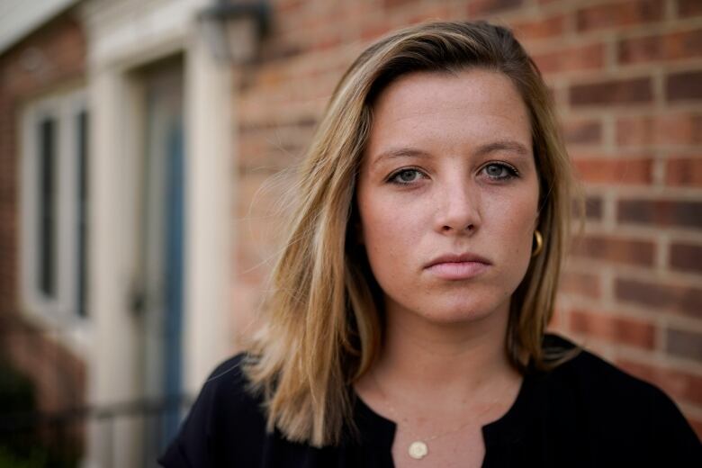 A woman looks at the camera with a serious look on her face outside a brick building