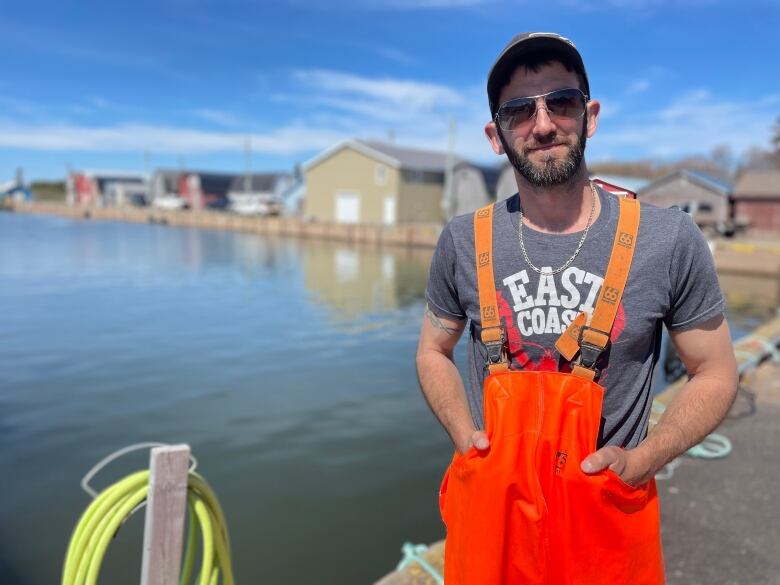 Fisherman in orange hip waders standing on wharf.