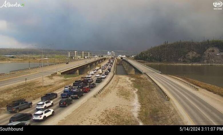 Three lanes of a highway show two empty and one packed with vehicles with smoky skies in the distance. 