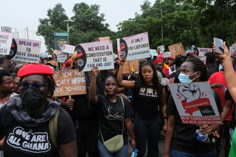 A large crowd of young people in Ghana hold signs and march. 